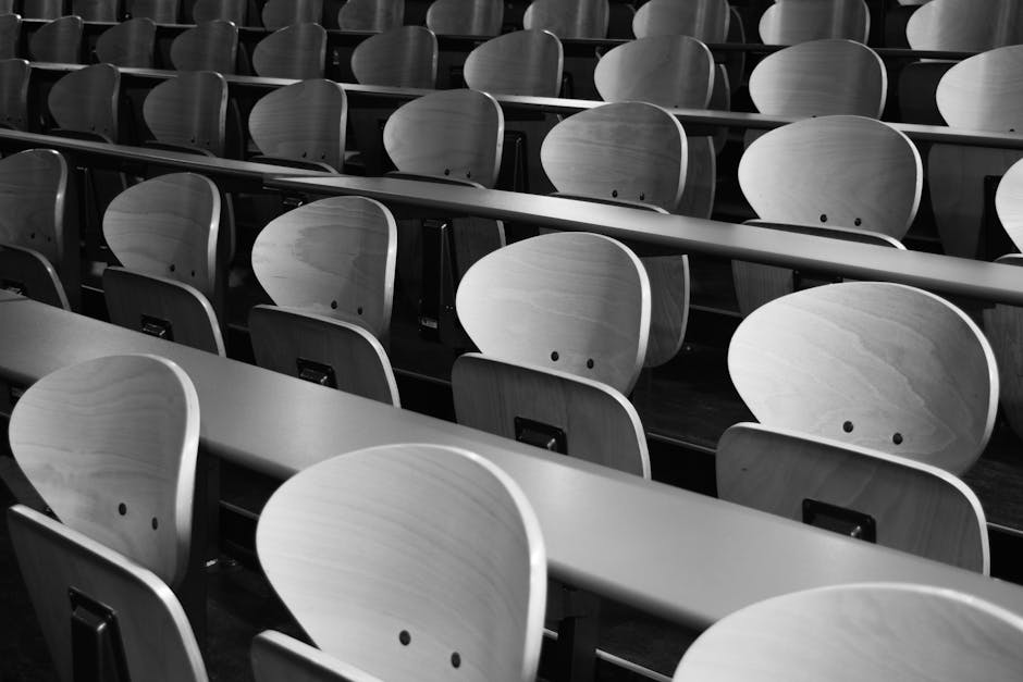 A monochrome view of empty wooden seats in a spacious lecture hall displaying symmetry and design